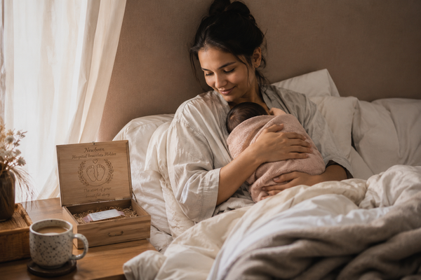 New mother in bed with a wooden keepsake box holding a hospital bracelet, tea going cold on the nightstand