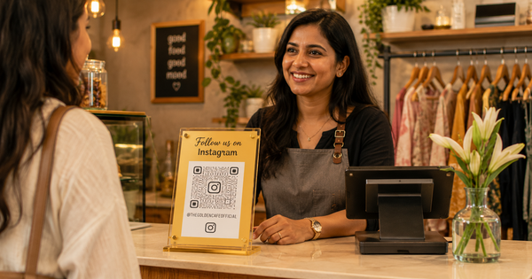 Happy Indian cafe or boutique owner with gold acrylic Instagram QR code stand on billing counter