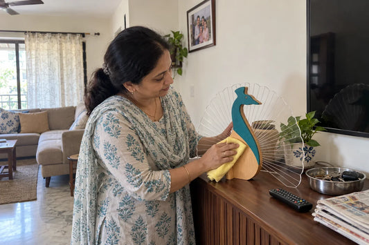 Woman wiping the Peacock wooden table lamp with a cloth on a living room console in daylight