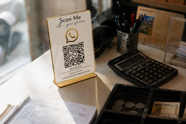 Custom acrylic WhatsApp QR code stand with gold border on a shop billing counter, WhatsApp icon and scannable QR code for instant customer chat