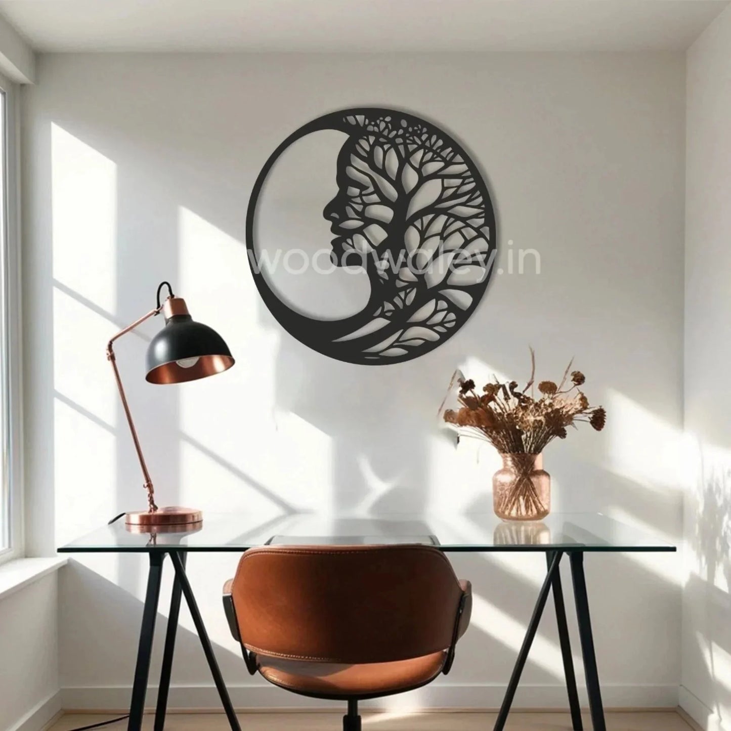 Modern home office with glass desk, brown chair, and black wooden moon tree wall art decor.